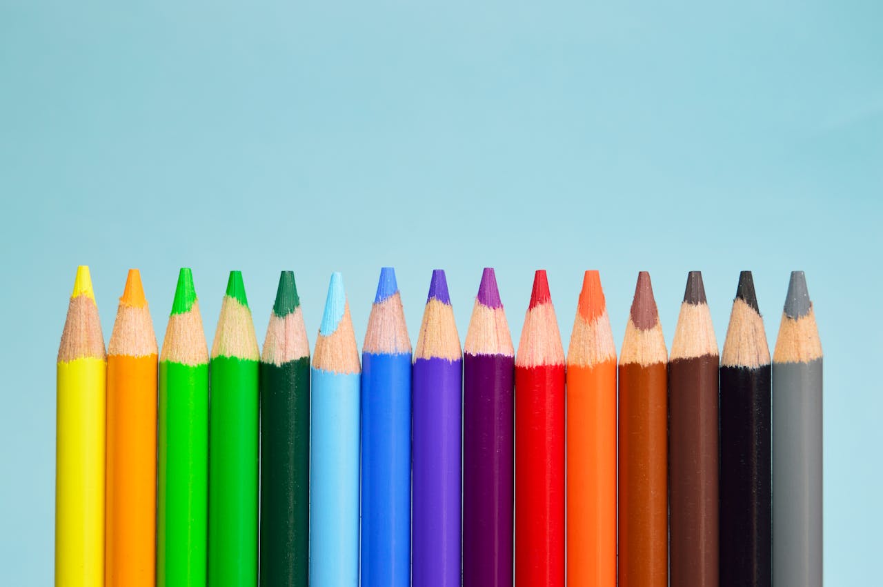 our-journey-01 A row of vibrant colored pencils lined up on a soft blue background, showcasing a spectrum of colors.
