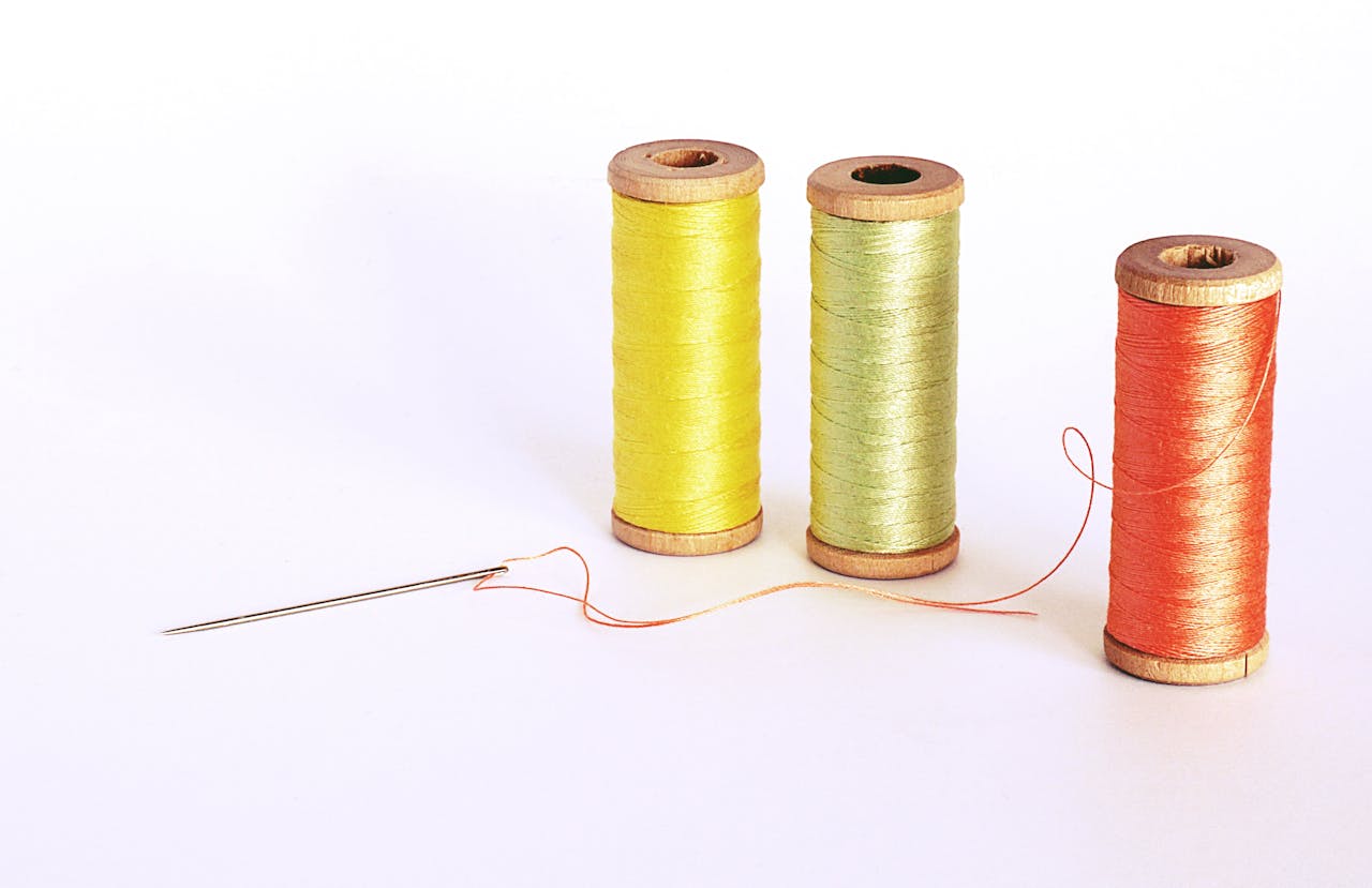 who-we-are Vibrant spools of thread with a needle on a white background depicting sewing craft.